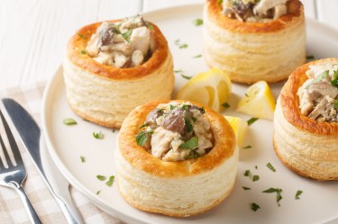 4 Blätterteig-Pasteten mit Pilzen auf einem Teller, daneben Messer und Gabel.