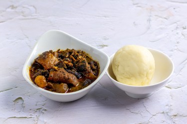 Eine Schüssel mit Fufu, einem Kloß aus Afrika, daneben eine Schüssel mit Spinateintopf.