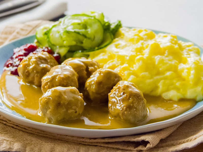 Eine Portion Körrbullar mit Dillgurken und Kartoffelpüree auf einem Teller.