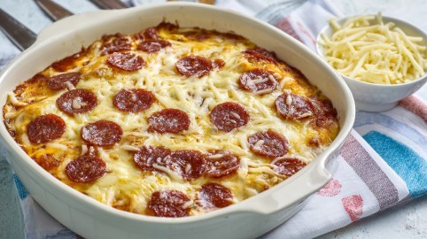 Pizza-Auflauf in weißer Auflaufform daneben eine Schale mit geriebenem Käse.