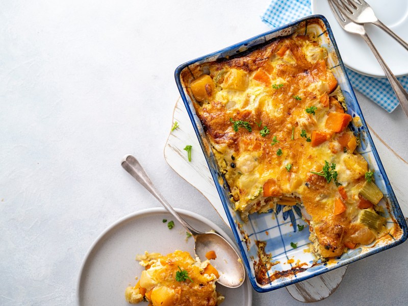 Eine Auflaufform mit Gemüseauflauf mit Béchamelsoße, und einem Teller daneben mit einem Stück des Auflaufs.