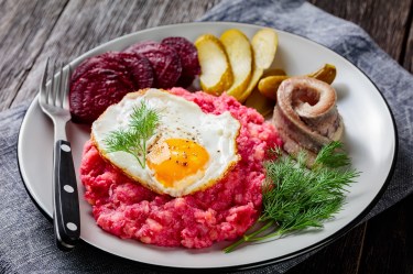 Hamburger Labskaus mit Spiegelei, Rollmops, Roter Bete und Gewürzgurken auf einem Teller, Nahaufnahme.