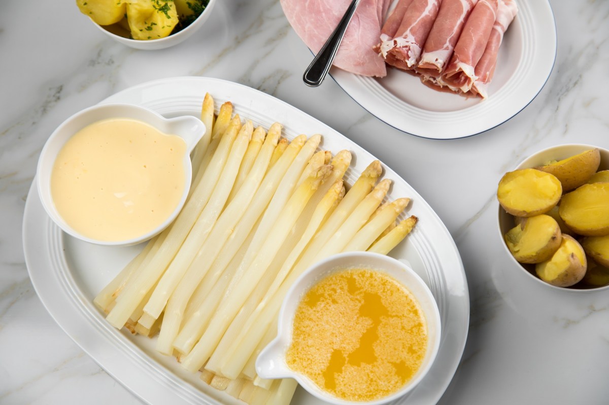 Teller mit weißem Spargel, Schinken, Kartoffeln und zwei Soßen.