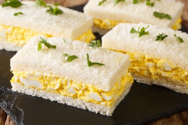 Mehrere japanische Ei-Sandwiches, Tamago Sando, auf einer Schieferplatte, garniert mit gehackter Petersilie.