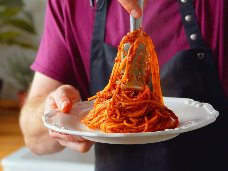 Ein Koche legt eine Potrion Spaghetti all'Assassina auf einen weißen Teller.