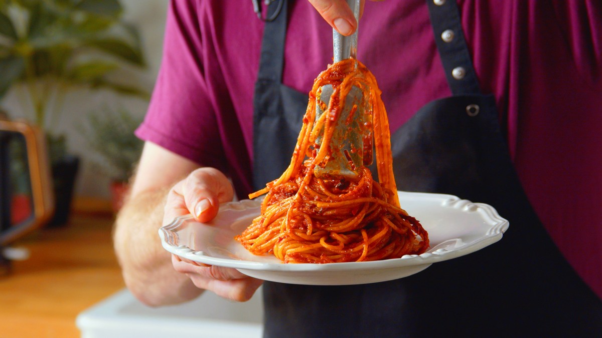 Ein Koche legt eine Potrion Spaghetti all'Assassina auf einen weißen Teller.