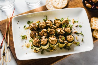 Zucchini-Röllchen mit Olivencreme auf einem Tablett.