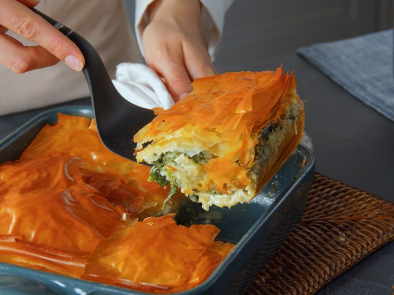 Ein Stück griechische Spinatpita wird mit einem Pfannenwender entnommen.
