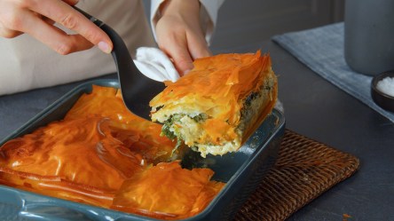 Ein Stück griechische Spinatpita wird mit einem Pfannenwender entnommen.