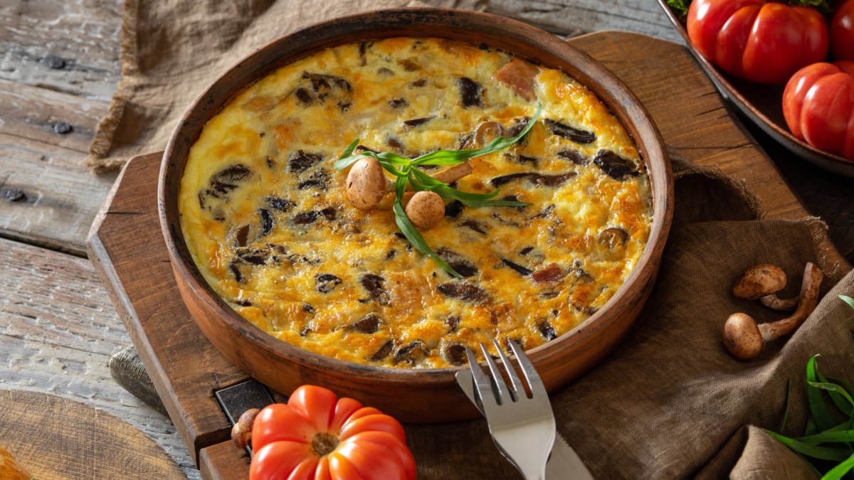 Eine Kartoffel-Frittata mit Pilzen in einer Pfanne. Drumherum liegen frische Zutaten.