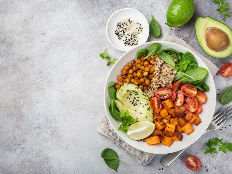 Kürbis-Quinoa-Bowl mit Kichererbsen und Avocado in der Draufsicht, drumherum Zutaten.