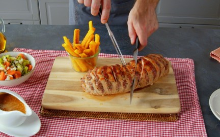 Ein gefüllter Schweinebraten wird mit einem Messer angeschnitten. Daneben Maispommes.