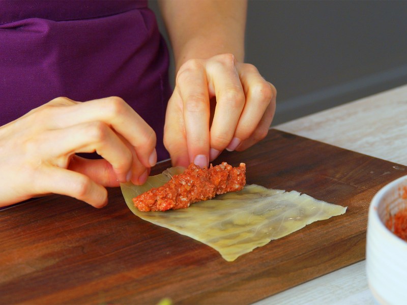 Eine Köchin rollt Hackfleischfüllung in ein blanchiertes Kohlblatt ein.