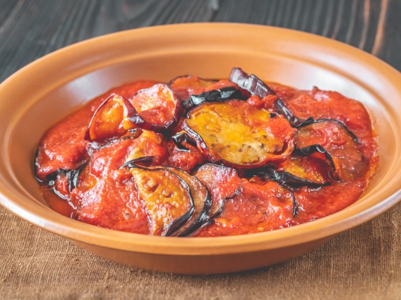 Eine Portion gebratene Aubergine in Tomatensoße in einem tiefen Teller.