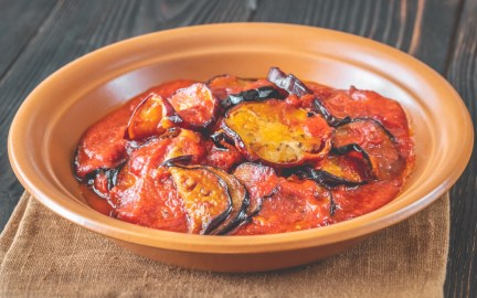 Eine Portion gebratene Aubergine in Tomatensoße in einem tiefen Teller.