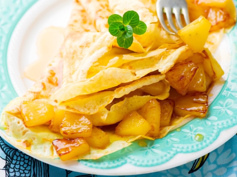 Kokoscrêpes mit karamellisierter Ananas auf einem Teller.
