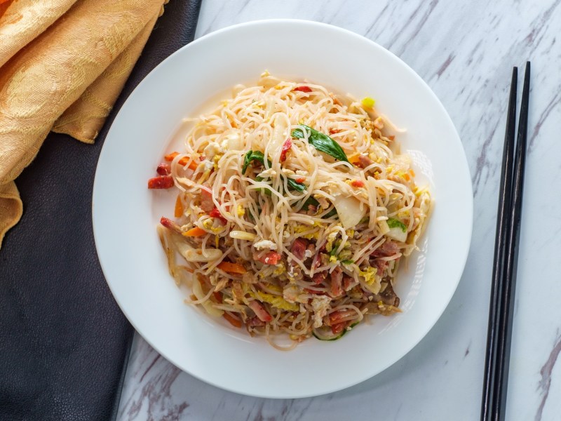 Ein Teller Mei Fun Nudeln mit Stäbchen daneben.