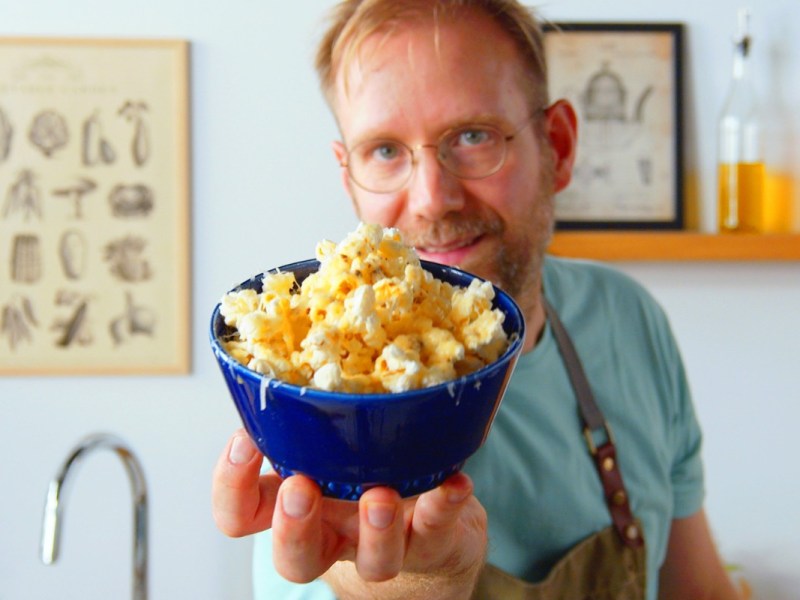 Ein Koch hält eine Schüssel Parmesan-Popcorn in die Kamera.