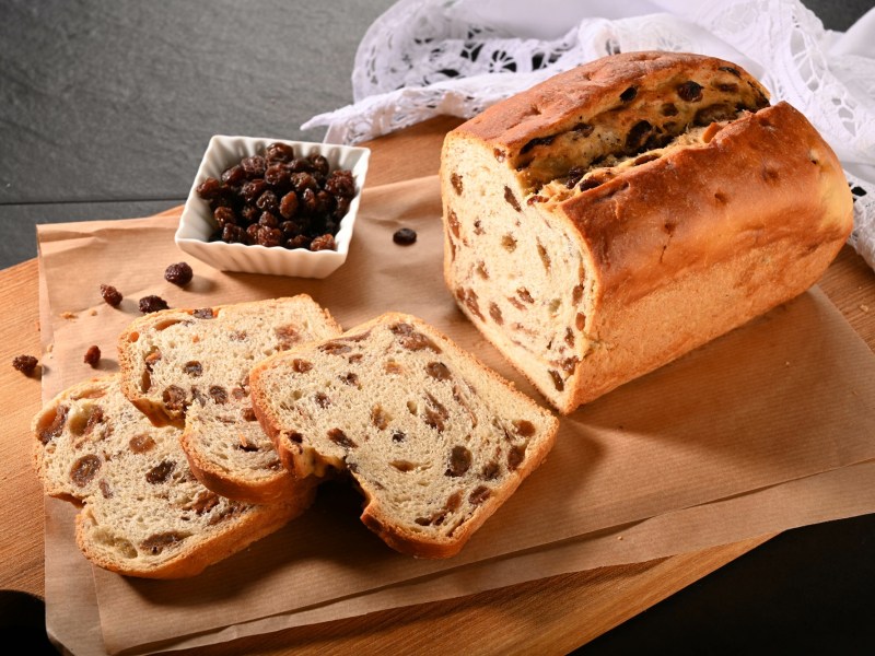 angeschnittener ostfriesischer Rosinenstuten auf einem Brett, Schale mit Rosinen daneben