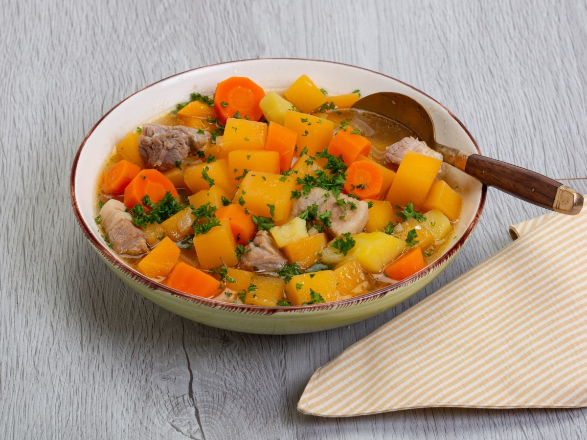Teller mit Steckrüben-Möhren-Eintopf auf einem Tisch, Stoffserviette daneben