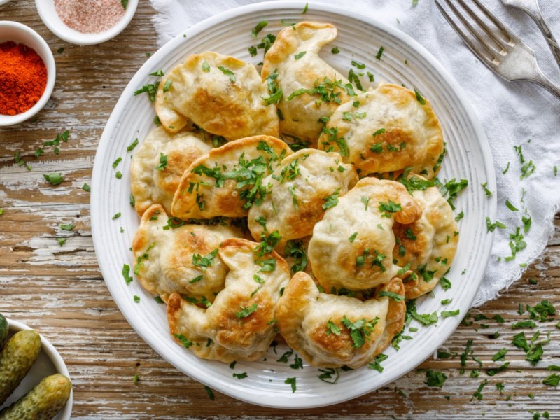 Mehrere Teigtaschen mit Pilz-Linsen-Füllung auf einem Teller in der Draufsicht.