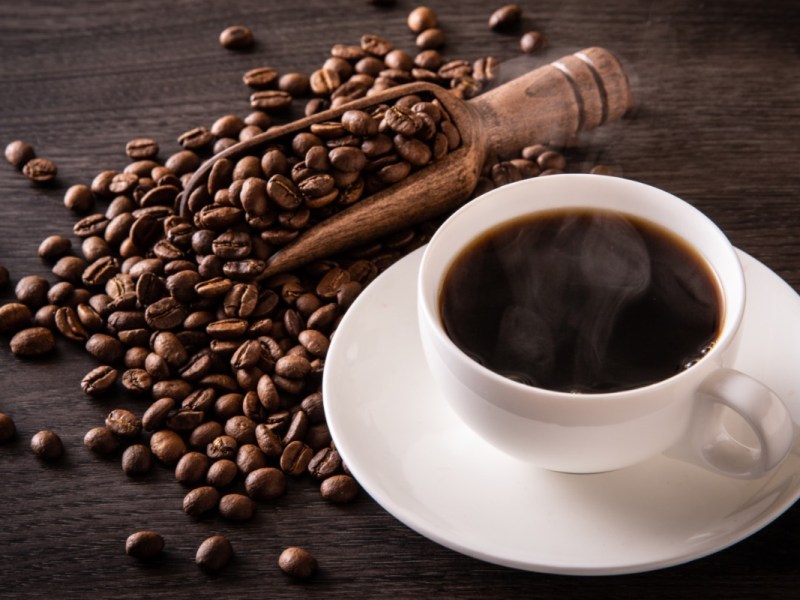 Wie wird Kaffee entkoffeiniert: Eine Tasse Kaffee neben der Kaffeebohnen liegen.