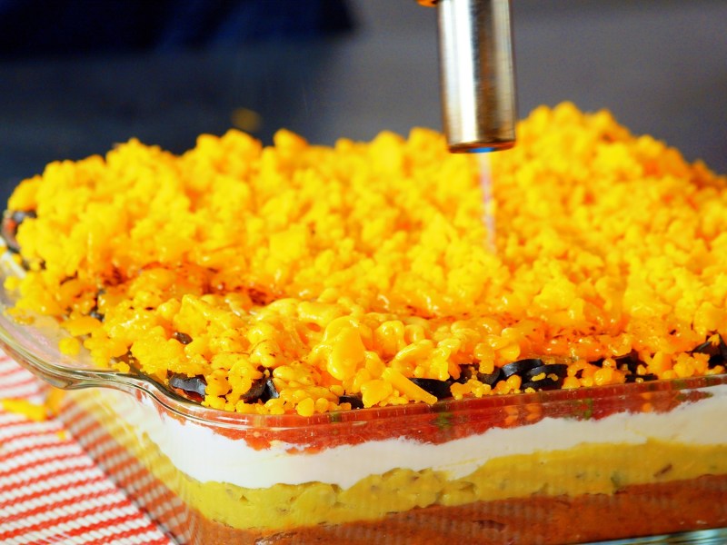 Seven-Layer-Dip: ein Koch schmilzt Cheddar mit einem Brenner.