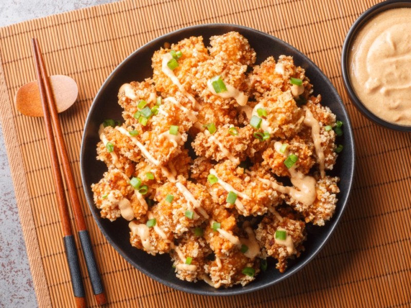 Bang Bang Chicken auf einem Teller in der Draufsicht. Daneben ein Schälchen mit Soße.