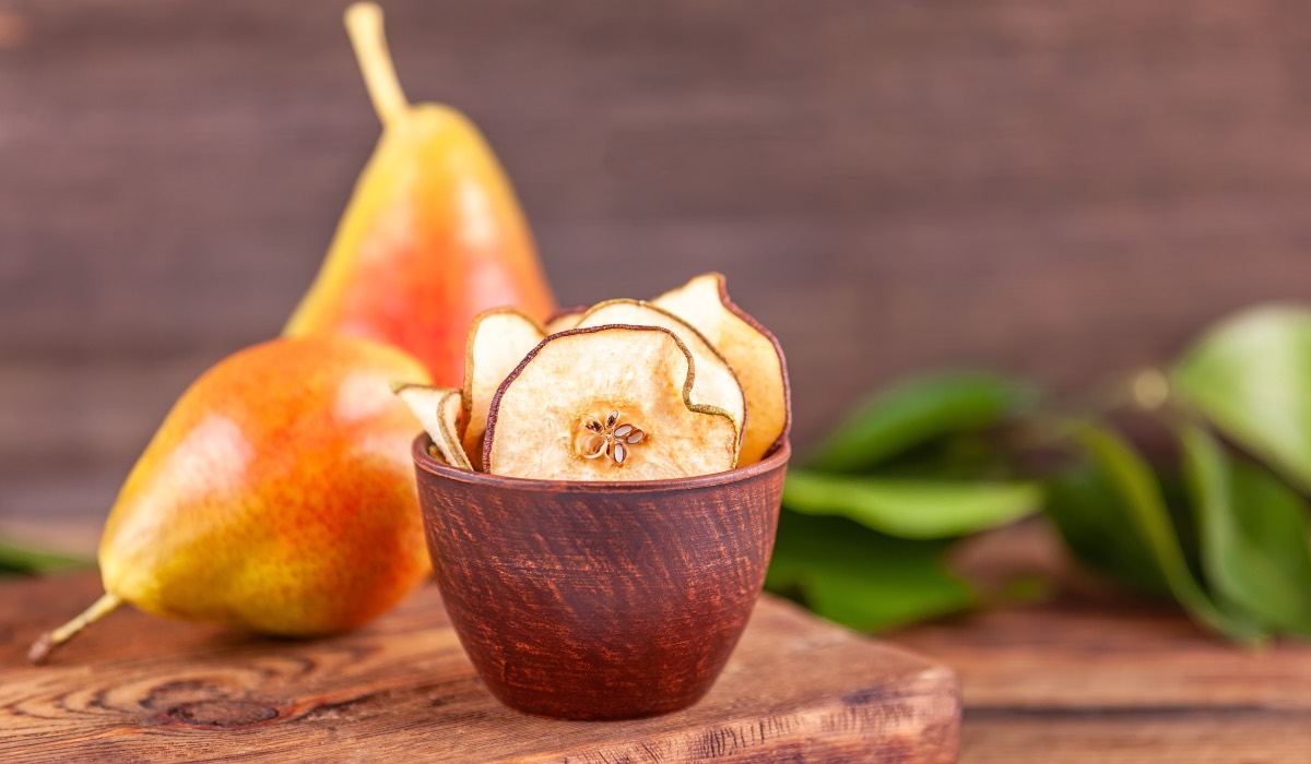 Ein Schälchen mit Birnenchips. Im Hintergrund liegen zwei frische Birnen.