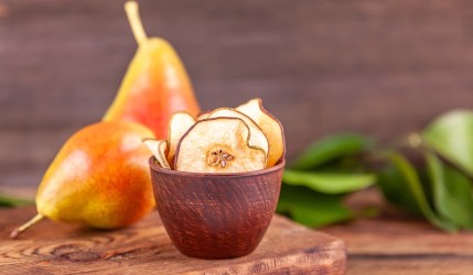 Ein Schälchen mit Birnenchips. Im Hintergrund liegen zwei frische Birnen.