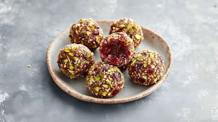 Ein kleiner Teller mit einigen Cranberry-Pistazien-Energy-Balls. Der Teller steht auf einer grauen Arbeitsfläche.