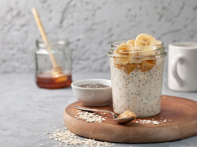 Ein Glas mit Erdnussbutter-Overnight-Oats. Im Hintergrund steht ein Glas Honig.
