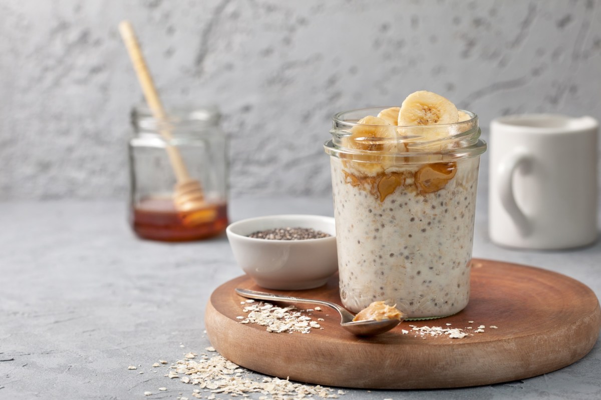 Ein Glas mit Erdnussbutter-Overnight-Oats. Im Hintergrund steht ein Glas Honig.
