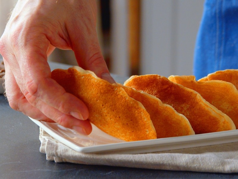 Mehrere gefüllte Pancakes auf einem Teller, einer wird von jemandem genommen.