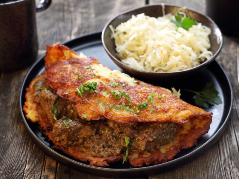 Ein Kartoffelpuffer mit Hackfleisch auf einem Teller. Daneben eine Schale mit Krautsalat.