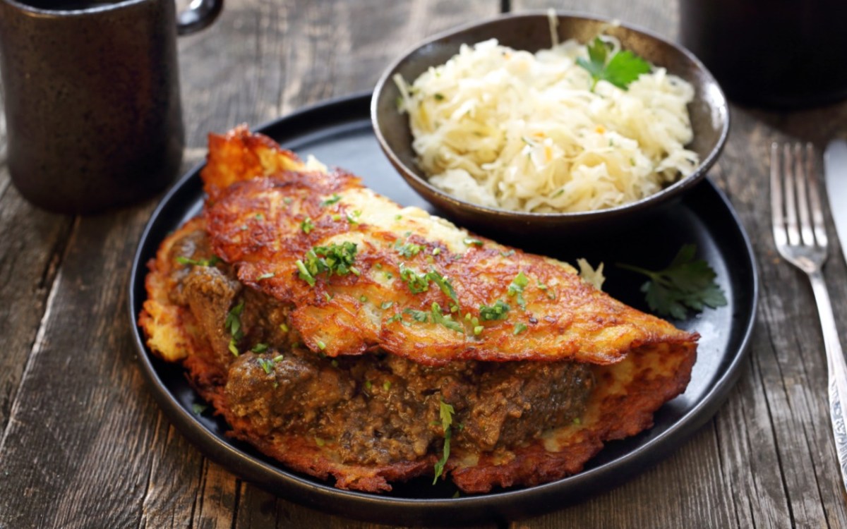 Ein Kartoffelpuffer mit Hackfleisch auf einem Teller. Daneben eine Schale mit Krautsalat.