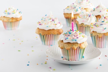 Mehrere Konfetti-Cupcakes mit Zuckerstreuseln verziert, in einem steckt eine brennende Kerze.