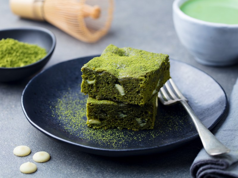 Teller mit zwei Stücken Matcha-Brownies, Gabel und Matcha-Pulver daneben