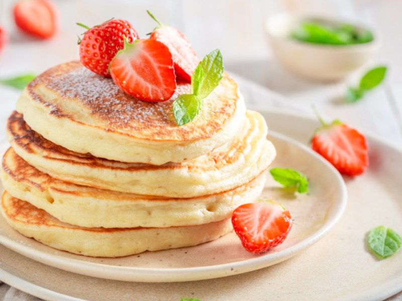 Ein Stapel Pancakes mit Buttermilch auf einem Teller, die mit Erdbeeren dekoriert sind.