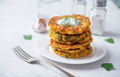Ein Stapel Pastinaken-Möhren-Puffer mit Dill und Petersilie. Obendrauf ist ein Klecks Joghurts.