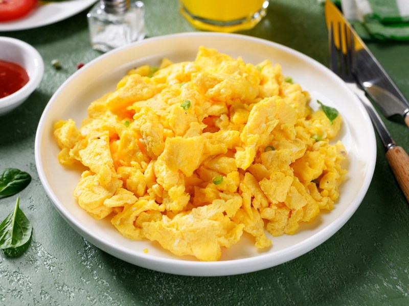 Ein Teller Rührei mit Parmesan, daneben Besteck, eine Schale Ketchup und ein Salzstreuer.