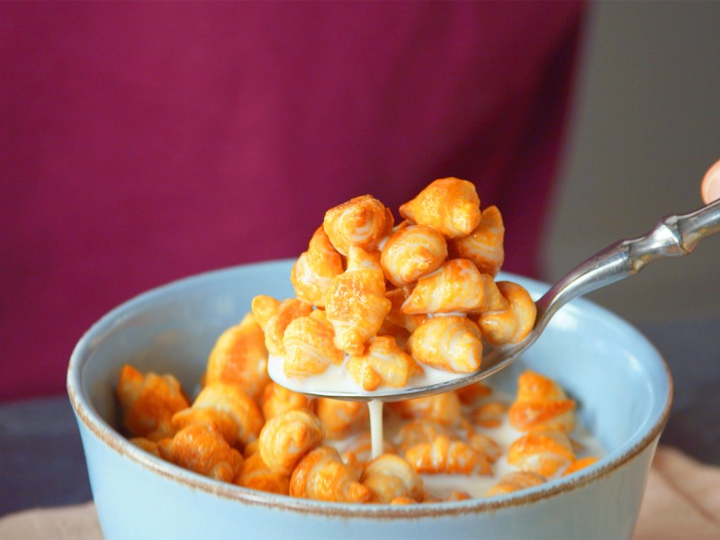 Eine Hand nimmt einen Löffel Schokocroissant-Müsli aus einer Müslischale.