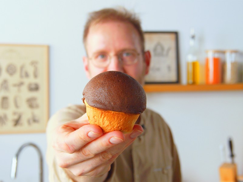 Ein Koch hält ein Schokoladen-Kaffeebrötchen in die Kamera.