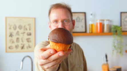 Ein Koch hält ein Schokoladen-Kaffeebrötchen in die Kamera.