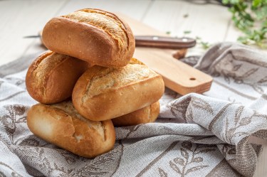 Ein paar Sonntagsbrötchen auf einem Geschirrtuch, dahinter ein Holzbrett.