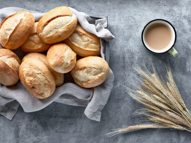 Ein Korb mit Übernacht-Brötchen, Weizeinbrötchen, in der Draufsicht, daneben eine Tasse Kaffee oder Getreideähren.