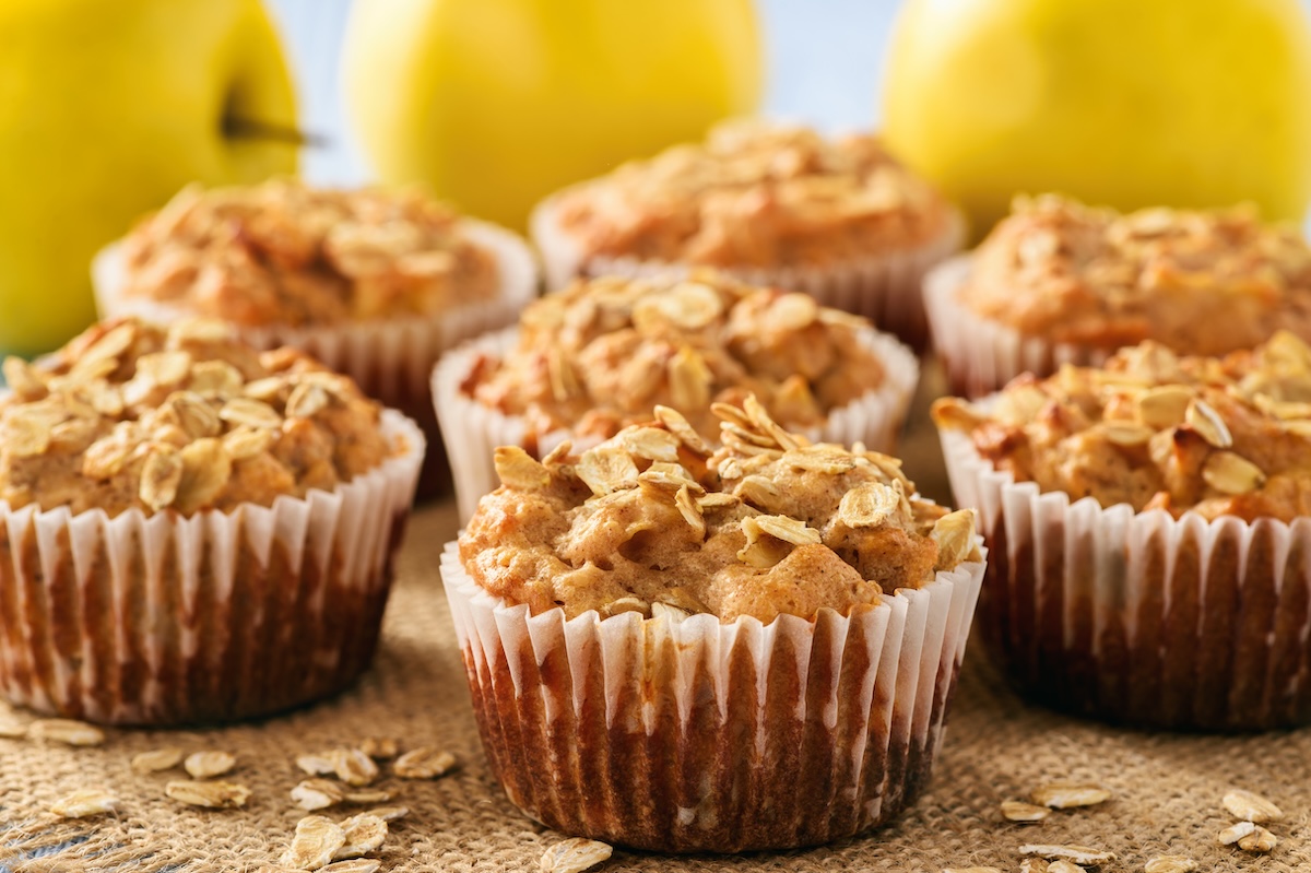 Apfel-Haferflocken-Muffins auf Holz, dahinter gelbe Äpfel.