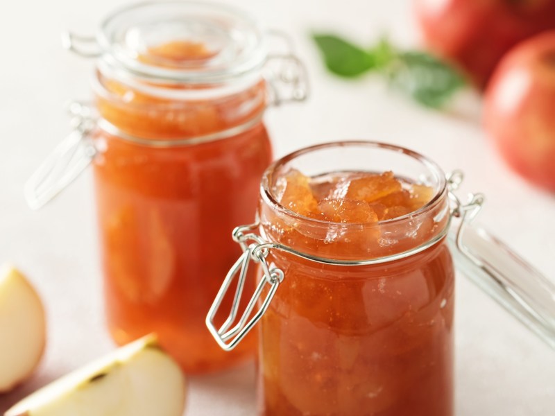 2 Gläser Apfelbutter, drumherum angeschnittene und ganze Äpfel.