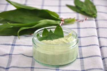 Eine kleine Glasschale Bärlauch-Curry-Aufstrich garniert mit Bärlauchblättern, im Hintergrund mehr Bärlauch.