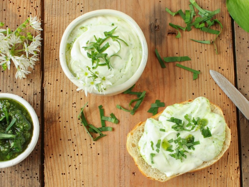 Glas und Stulle mit Bärlauchaufstrich samt Messer auf Holz-Untergrund.